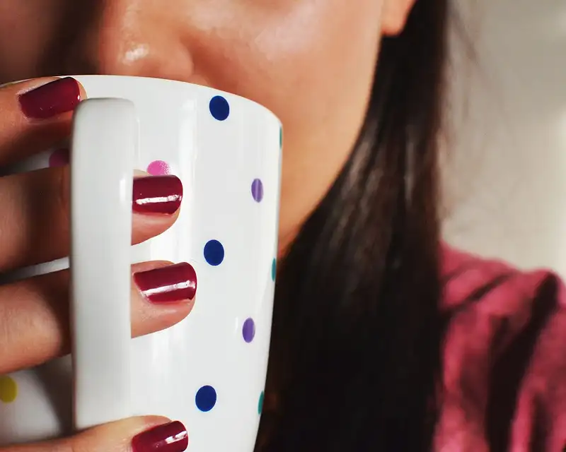Des ongles vernis rouge cerise posés sur une tasse blanche à pois.
